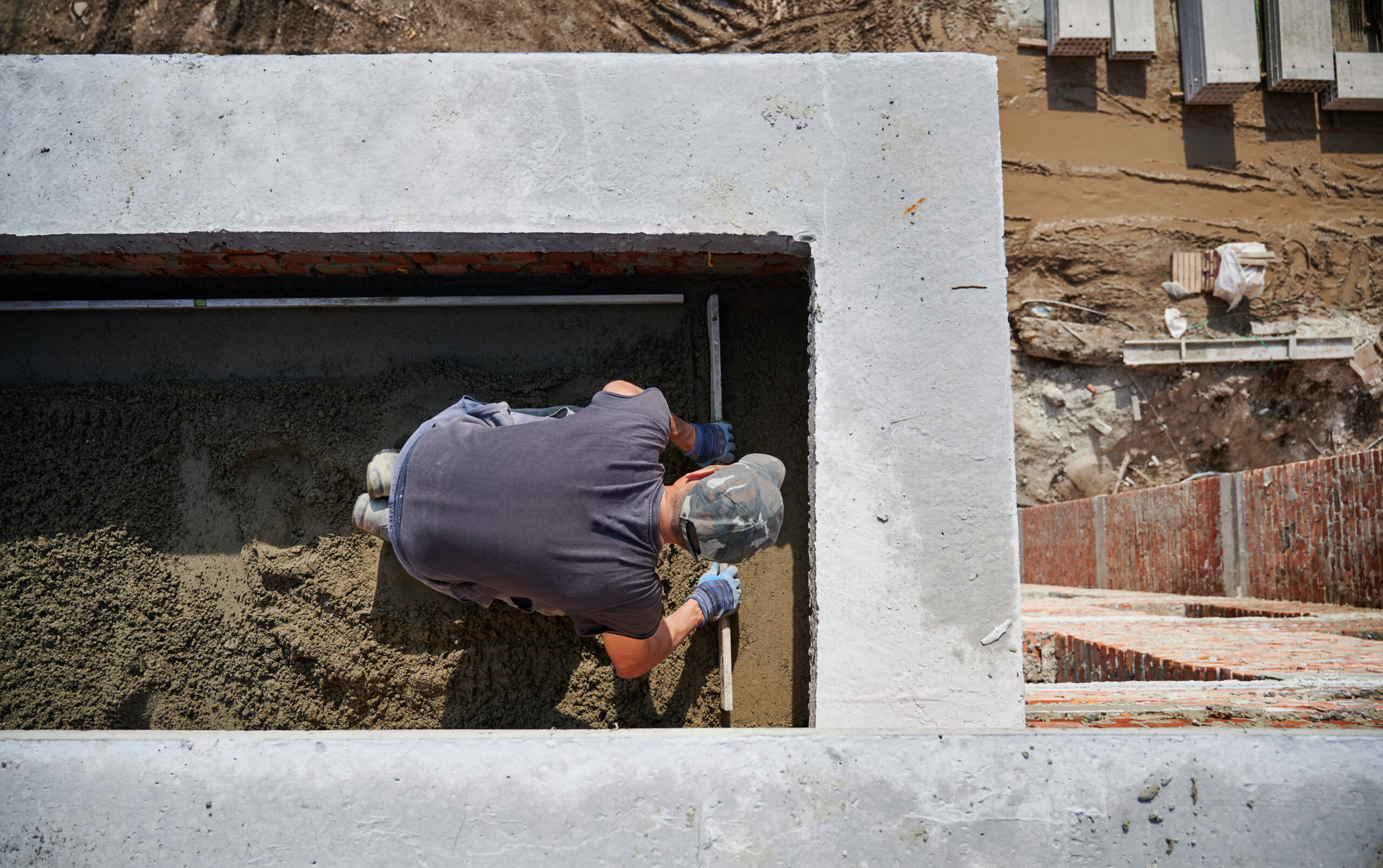 Top view of bricklayer in protective gloves working with sand and doing walls on fresh air. Concept of process building walls and modern house with good weather and modern equipments.
